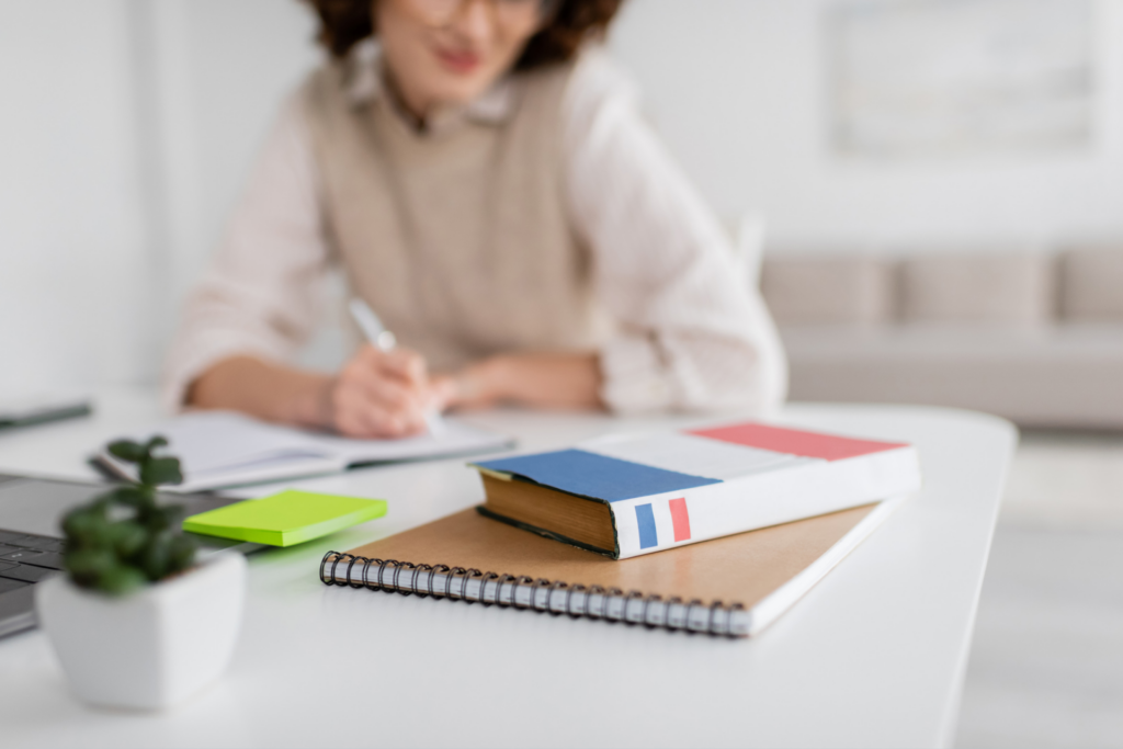 Mujer enfocada aprendiendo francés en su escritorio, con un libro de francés abierto en frente de ella, evidenciando el progreso que se puede hacer al aprender francés