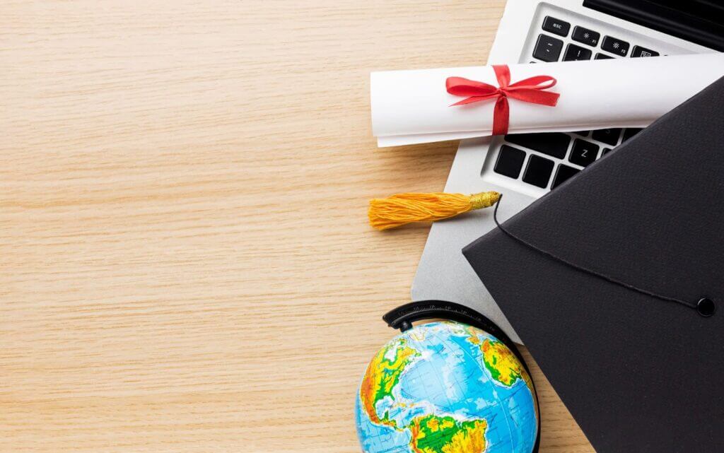 Escritorio con diploma, computadora, birrete y globo terráqueo.